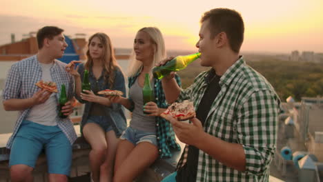 Amorosas-Parejas-Jóvenes-Rusas-Se-Sientan-En-El-Techo-Y-Beben-Cerveza-Con-Pizza.-Disfrutan-De-Una-Hermosa-Puesta-De-Sol-Y-De-Tiempo-Con-Su-Pareja.